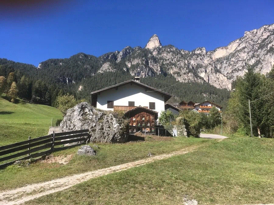 An alpine house beneath forested cliffs and rocky peaks on a clear day